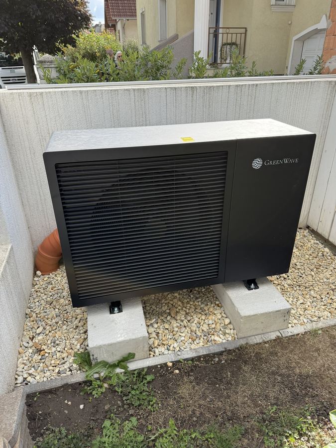 Schwarze Monoblock-Wärmepumpe auf zwei Betonsockeln im Kiesbett