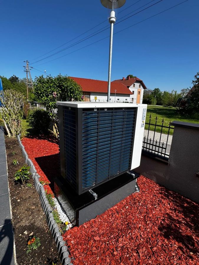Fertig montierte Wärmepumpen-Außeneinheit im Garten auf einem Streifen aus rotem Rindenmulch